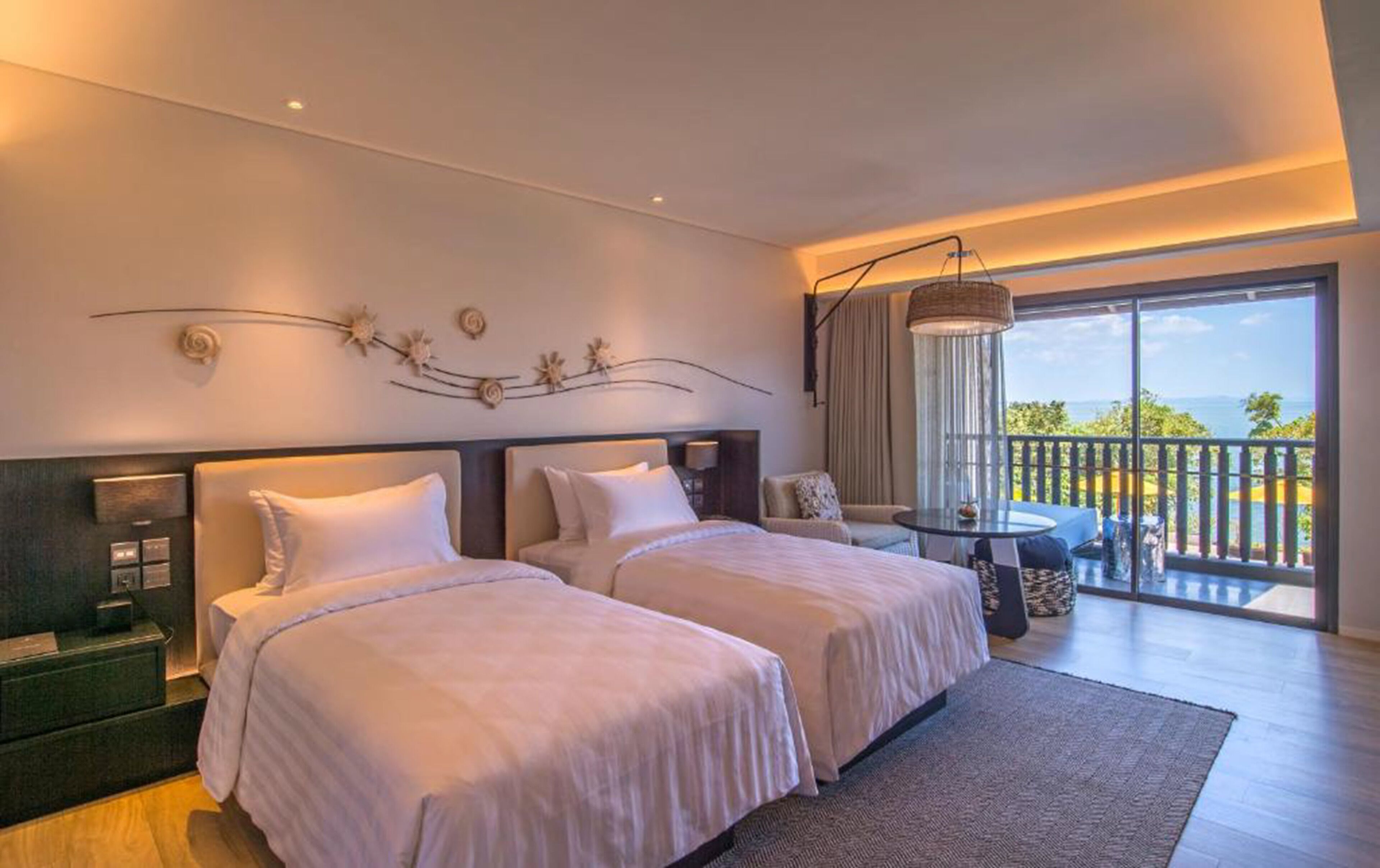 A hotel room with two beds, a small table, and a balcony with a view.
