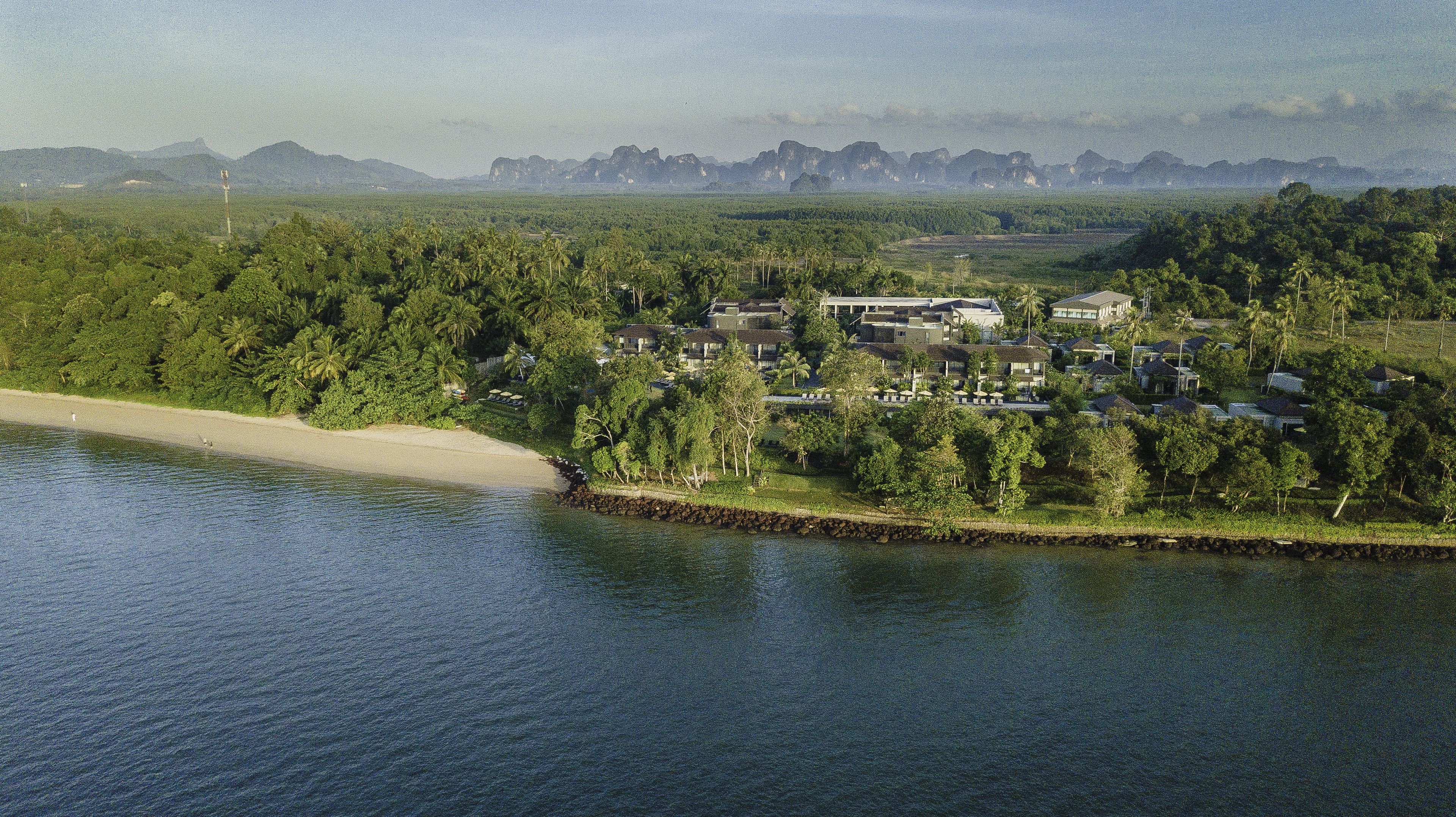 A coastal property with a beach, dense greenery, and a view of distant mountains.