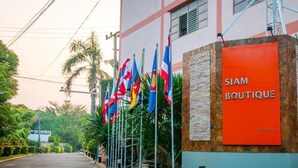 A building with multiple flags, a sign reading "SIAM BOUTIQUE," and a stone wall. - Siam Boutique (Buriram)