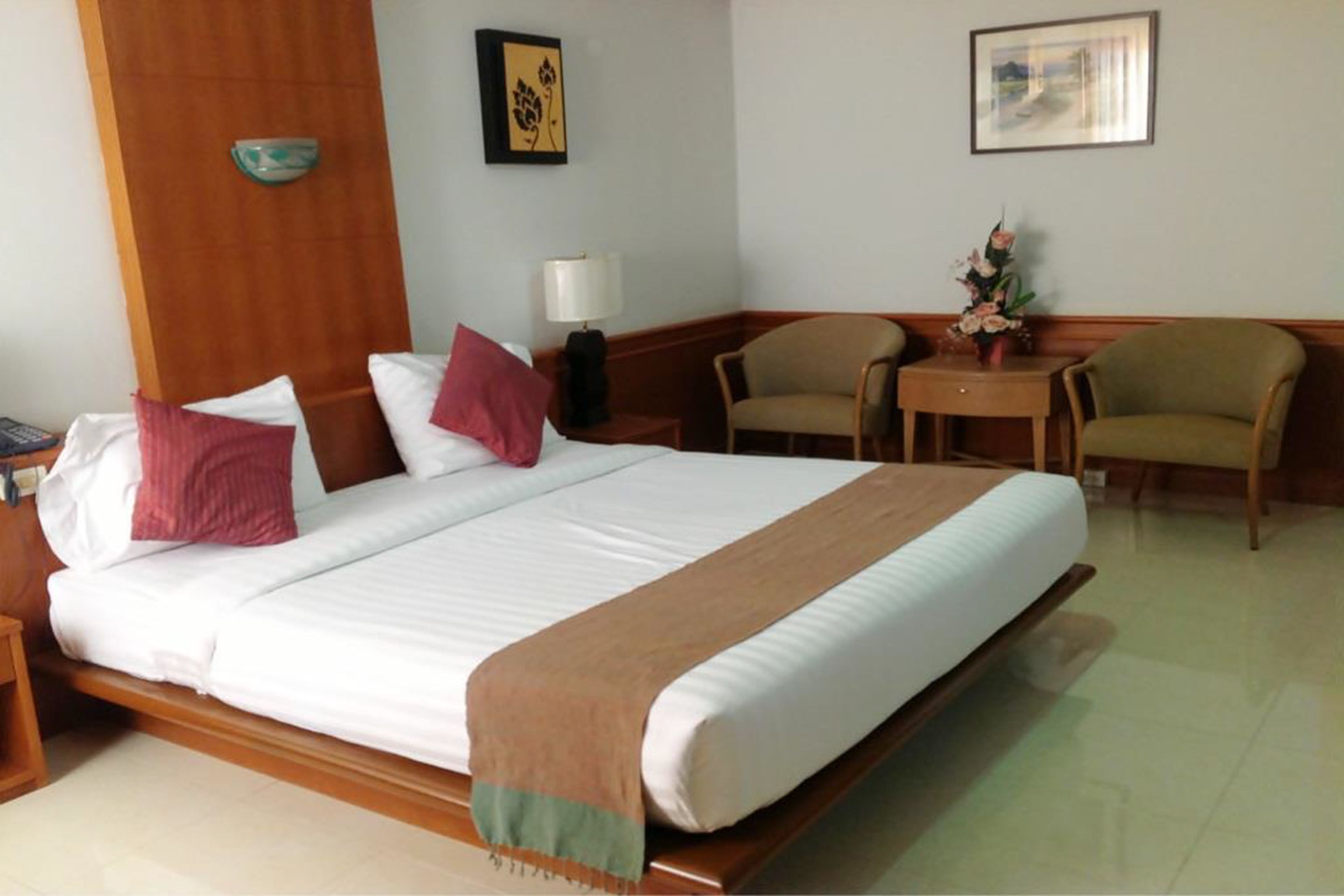 Una habitación de hotel con una cama grande, dos sillas, una mesita y una lámpara de pared.