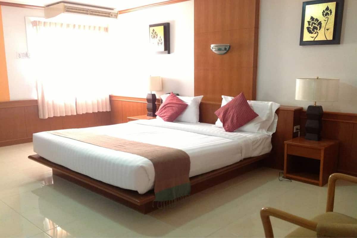 A hotel room with a large bed, wooden headboard, two bedside tables with lamps, and a window with curtains.
