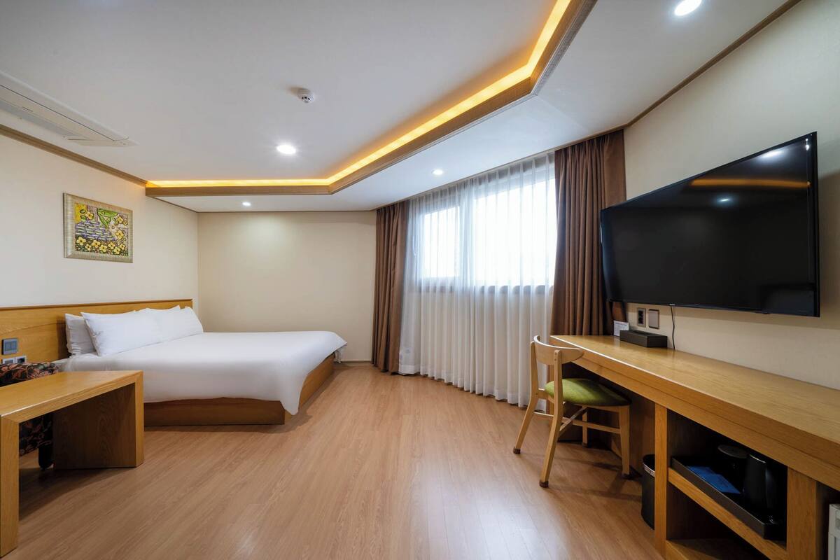 Una habitación de hotel con cama, escritorio, televisor y cortinas.