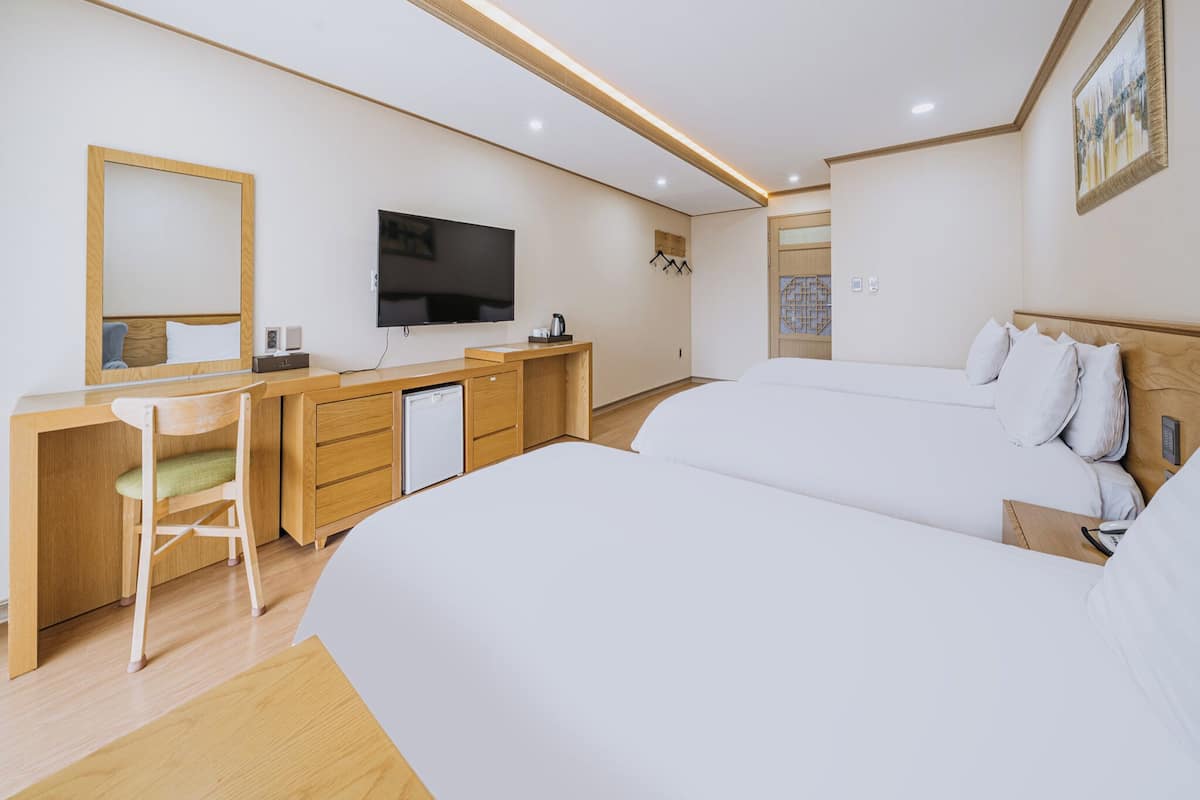 Una habitación de hotel con dos camas, un escritorio con silla, un televisor y un mueble pequeño.