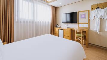 A hotel room with a bed, a desk with a TV, a chair, and a robe rack.
