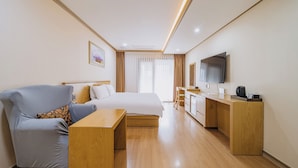 A hotel room with a bed, a seating area, a desk, a TV, and a window with curtains. - Nohyung Hotel (Jeju City)