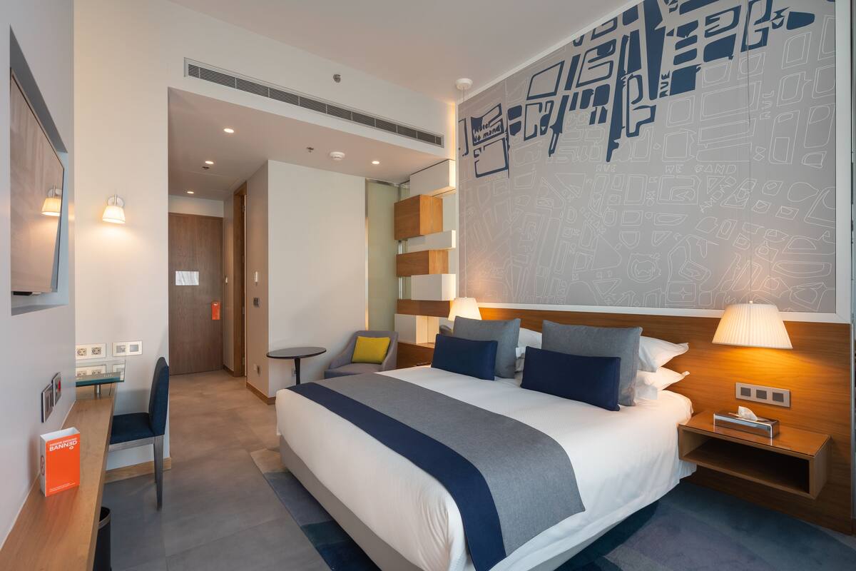 A modern hotel room with a large bed, bedside tables, a desk, and a chair.