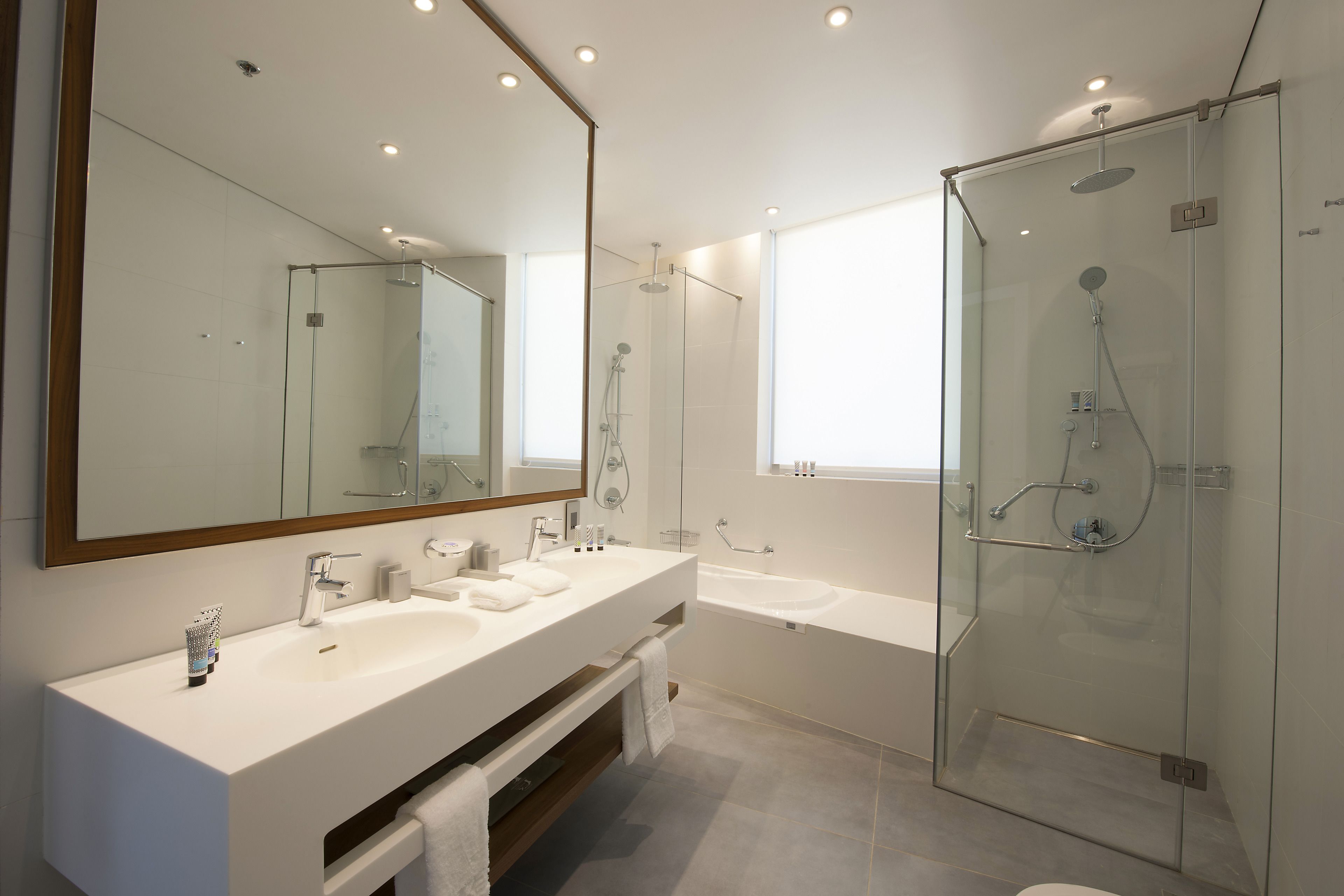 Un baño moderno con un espejo grande, dos lavamanos, una bañera y una ducha con paredes de vidrio.