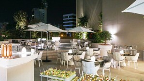 Un espacio al aire libre para comer con varias mesas y sillas, sombrillas y una mesa de bufé con aperitivos.
