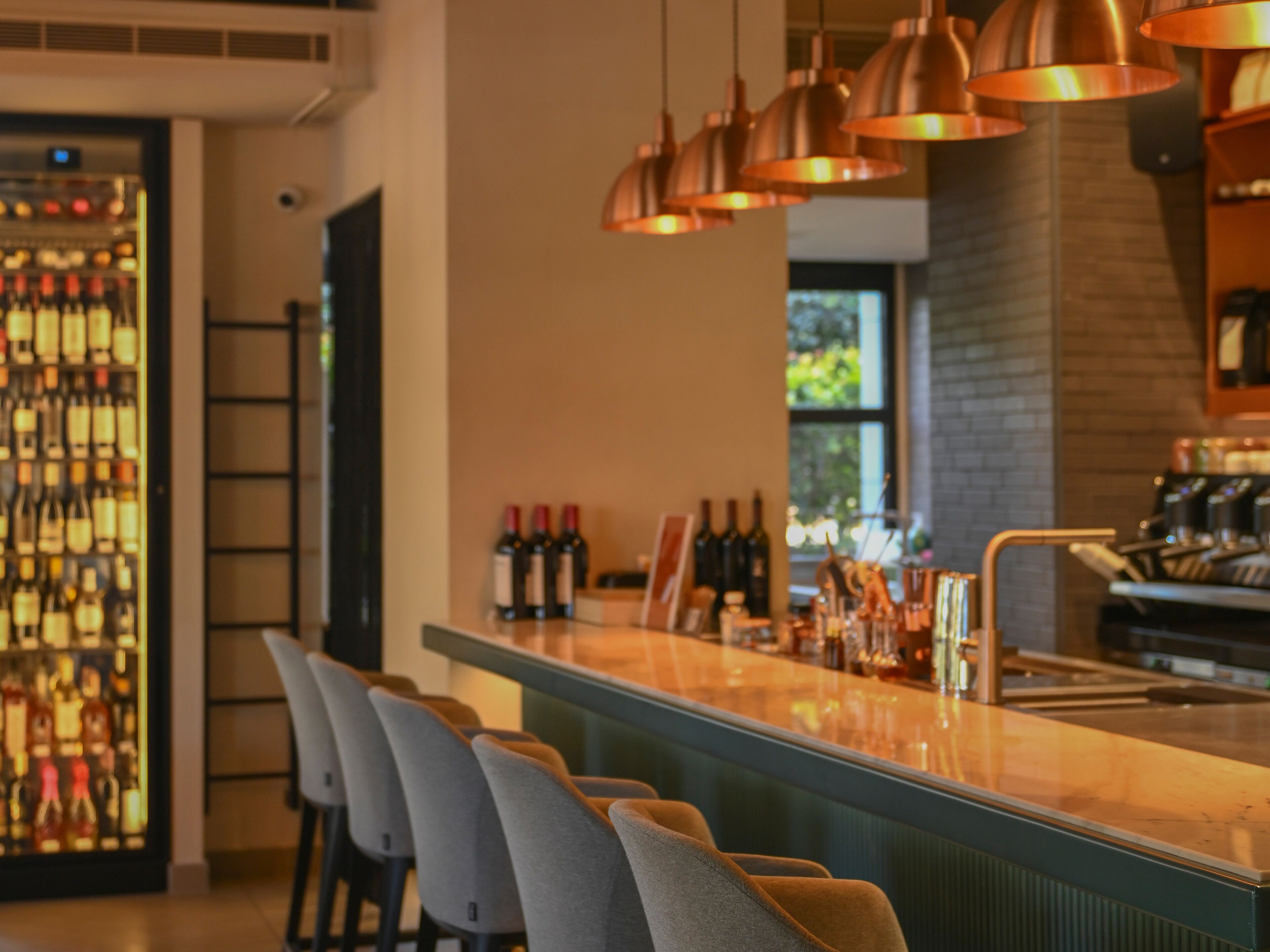 A bar area with a long counter, several chairs, and hanging copper pendant lights.