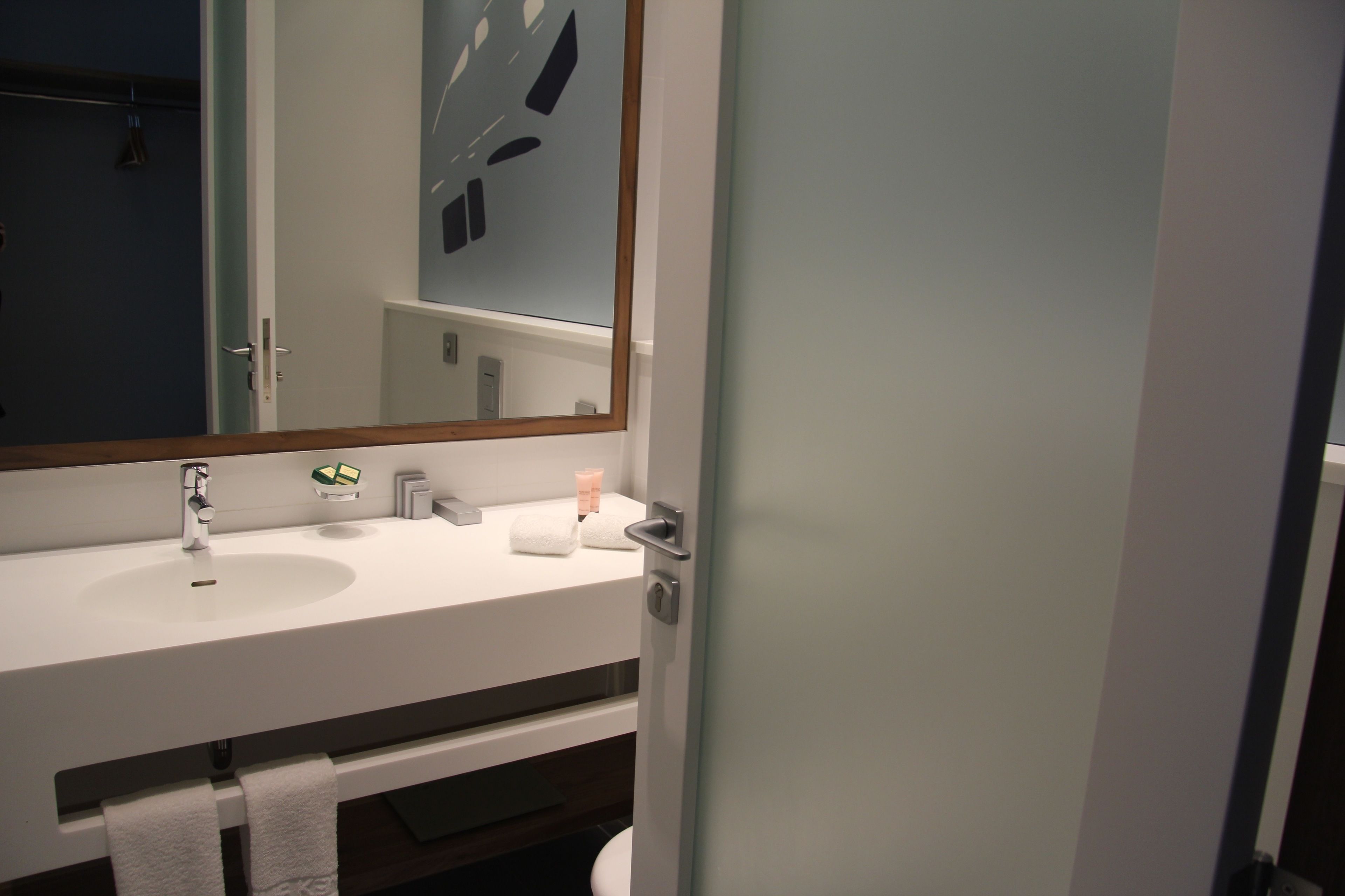 Une salle de bain moderne avec un lavabo blanc, un grand miroir et un porte-serviettes.