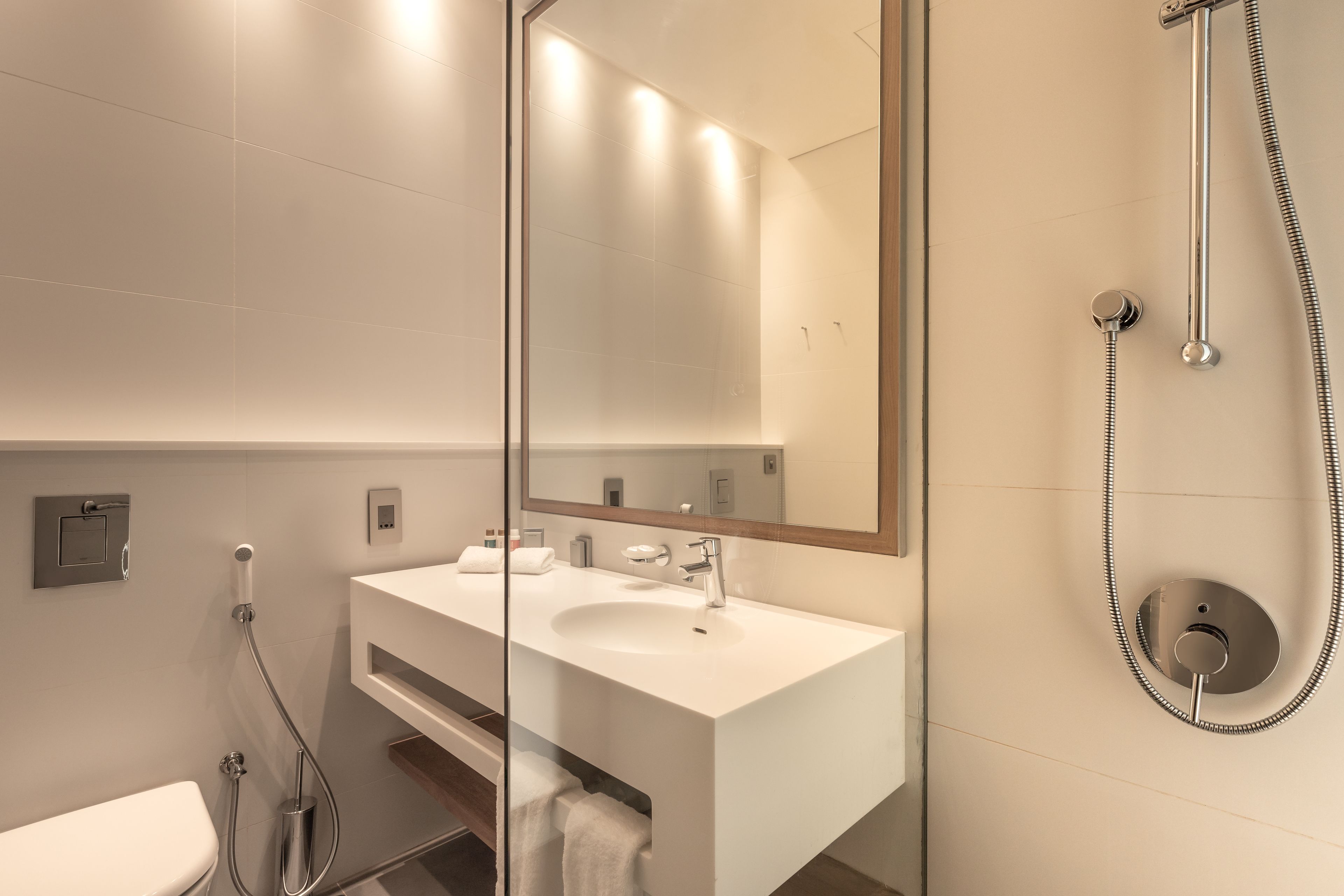 Un baño moderno con un lavamanos blanco, un espejo grande y una ducha con cabezal de ducha de mano.