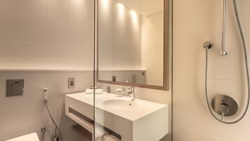 Un baño moderno con un lavamanos blanco, un espejo grande y una ducha con cabezal de ducha de mano.