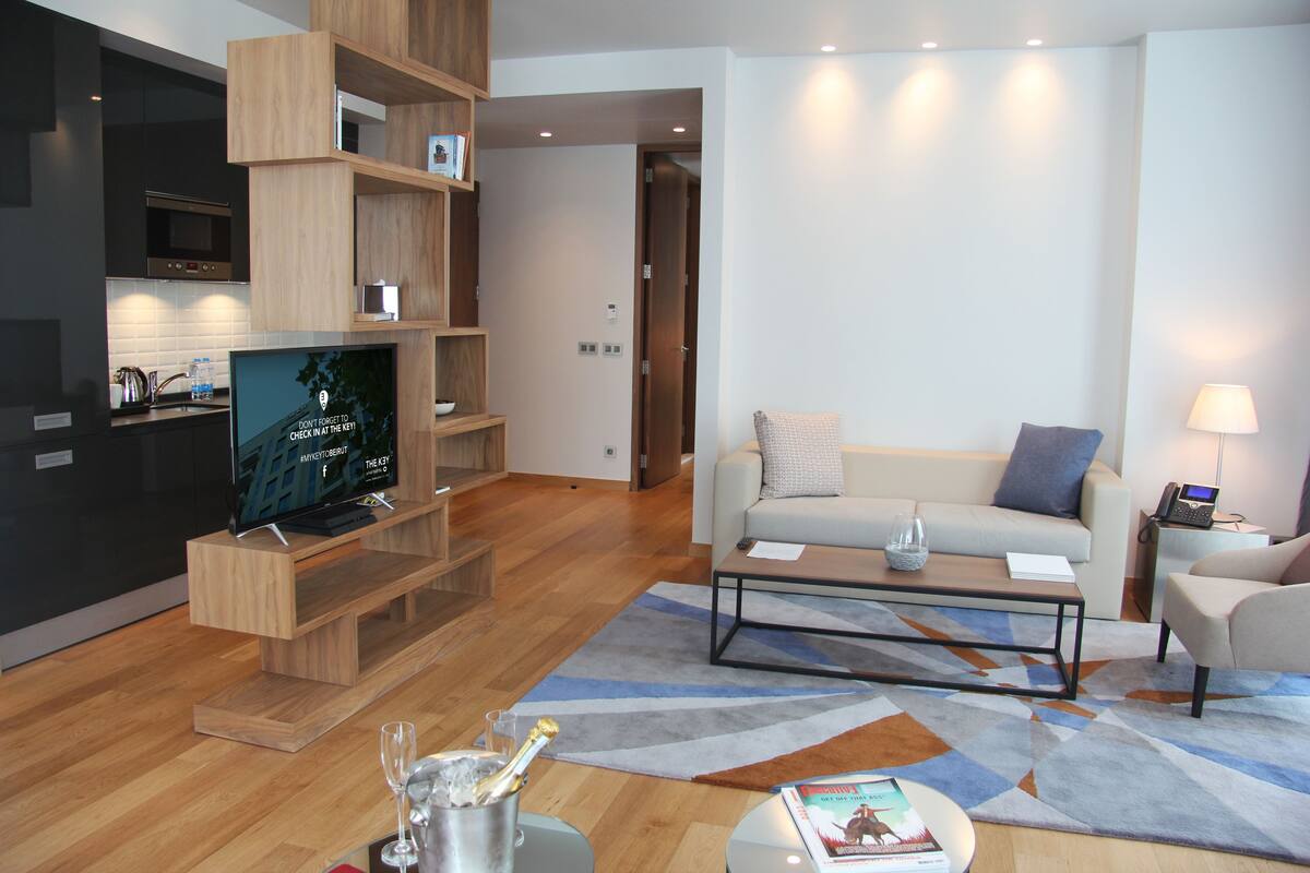 A modern living room with a flat-screen TV, wooden shelving, a sofa, a coffee table, and a lamp.