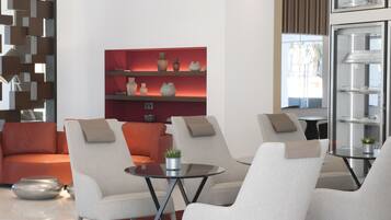 A modern living room with a sofa, armchairs, a glass coffee table, and a red shelving unit with decorative items.