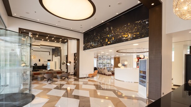 Un moderno vestíbulo de hotel con piso a cuadros, un mostrador de recepción y un mural con vista a la ciudad.