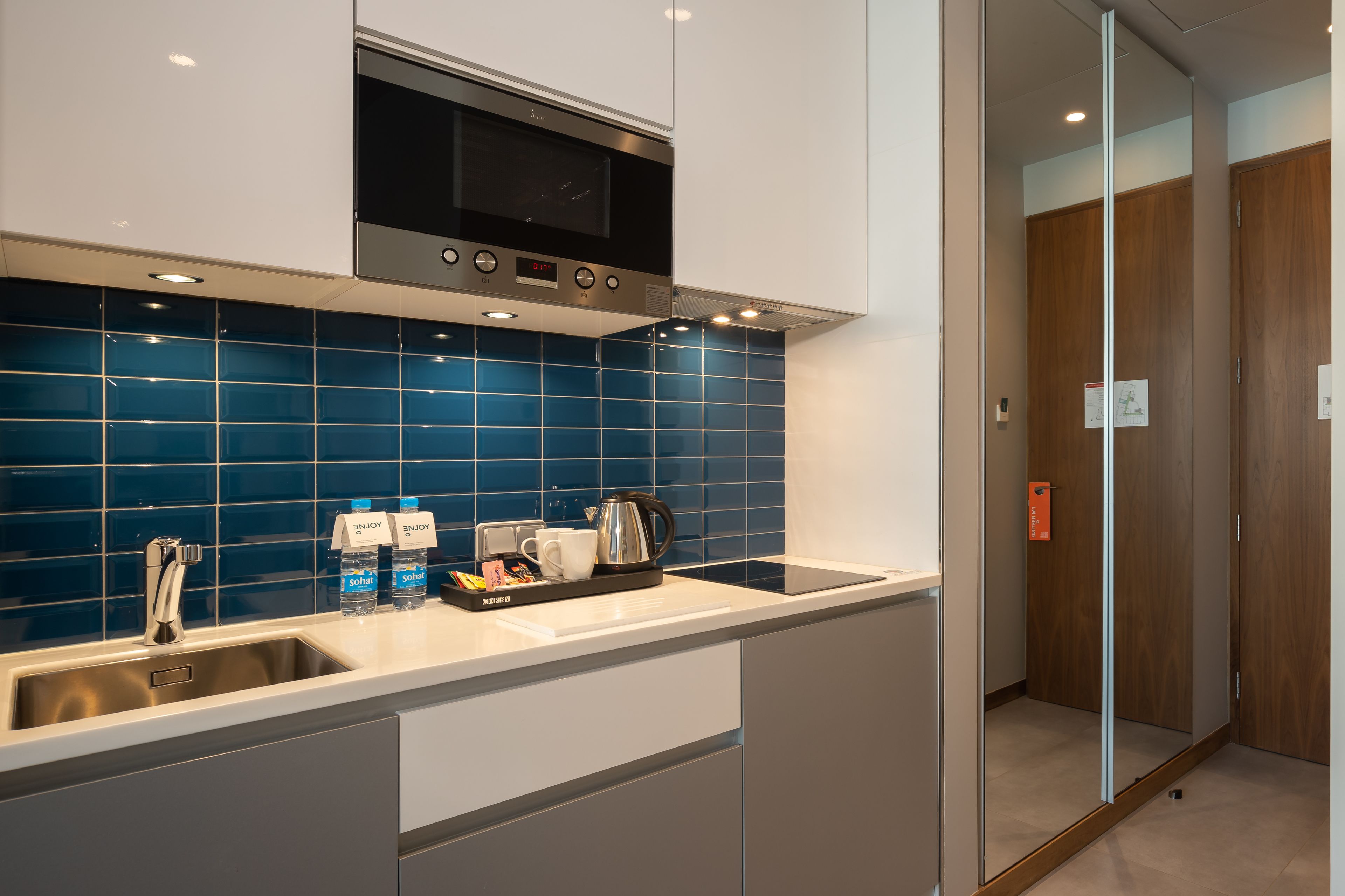 A modern kitchen with a stainless steel microwave, a sink, and a tray with coffee and water bottles.