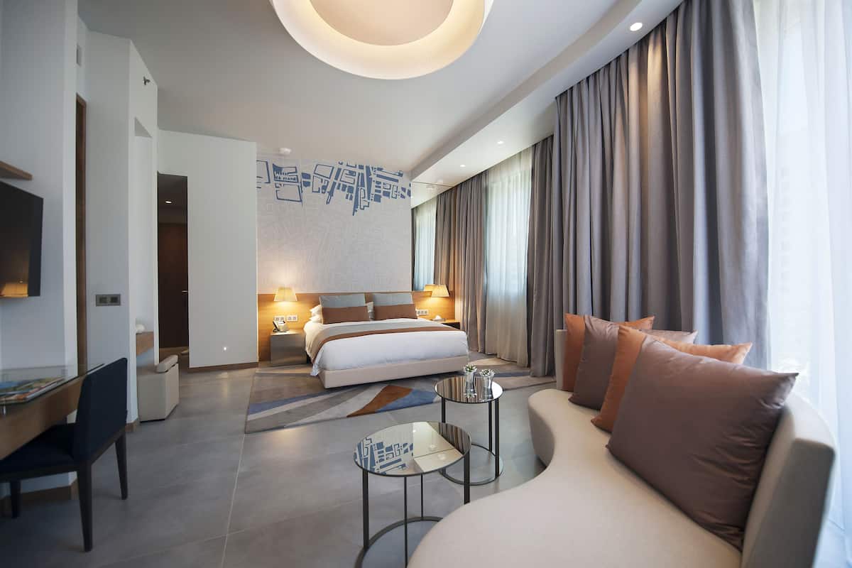 A modern hotel room with a large bed, a sofa, a desk, and a TV.
