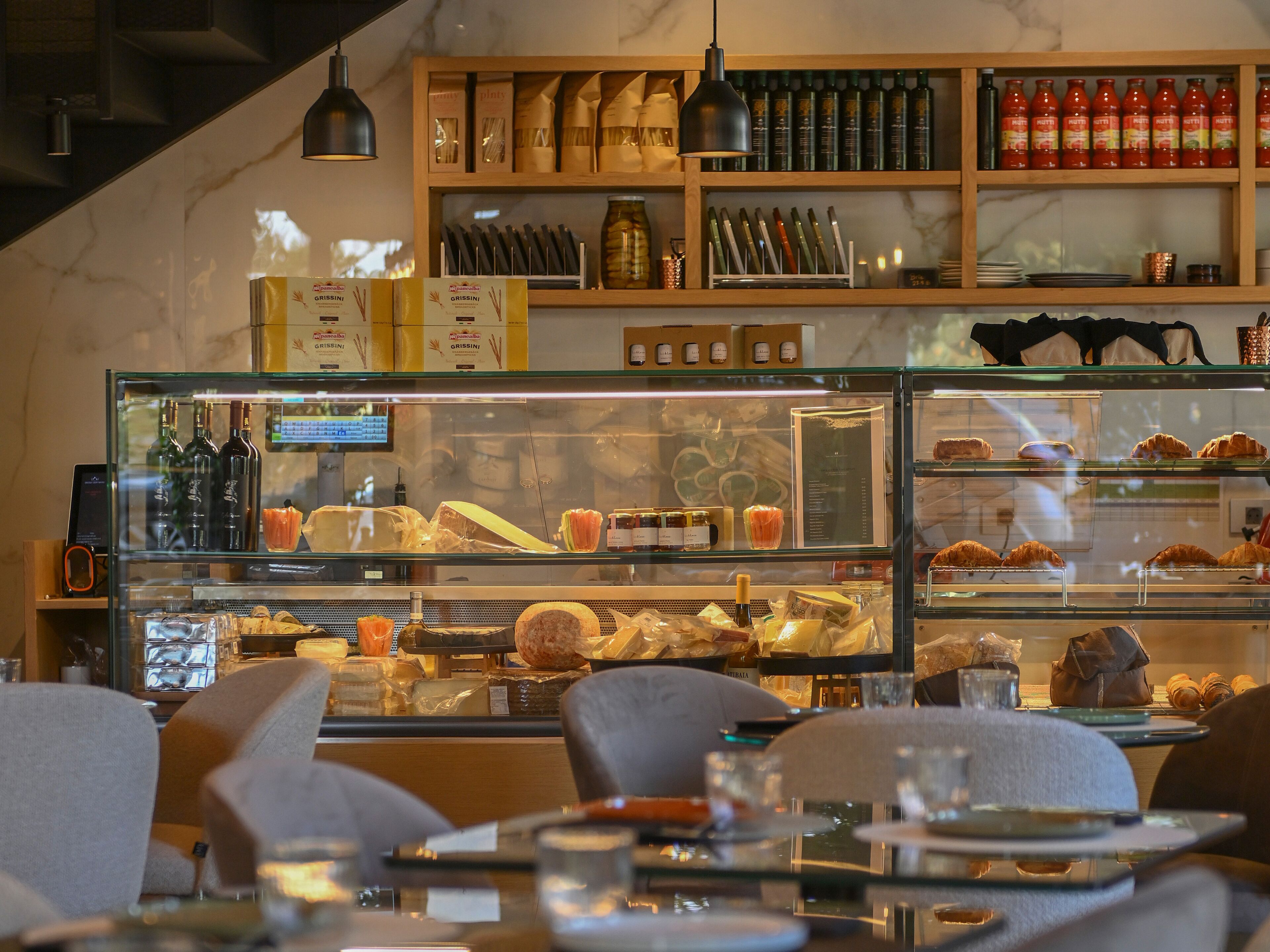L’intérieur d’un restaurant présente une vitrine en verre où sont exposés des produits alimentaires, une étagère en bois où sont rangés des condiments et un luminaire suspendu.