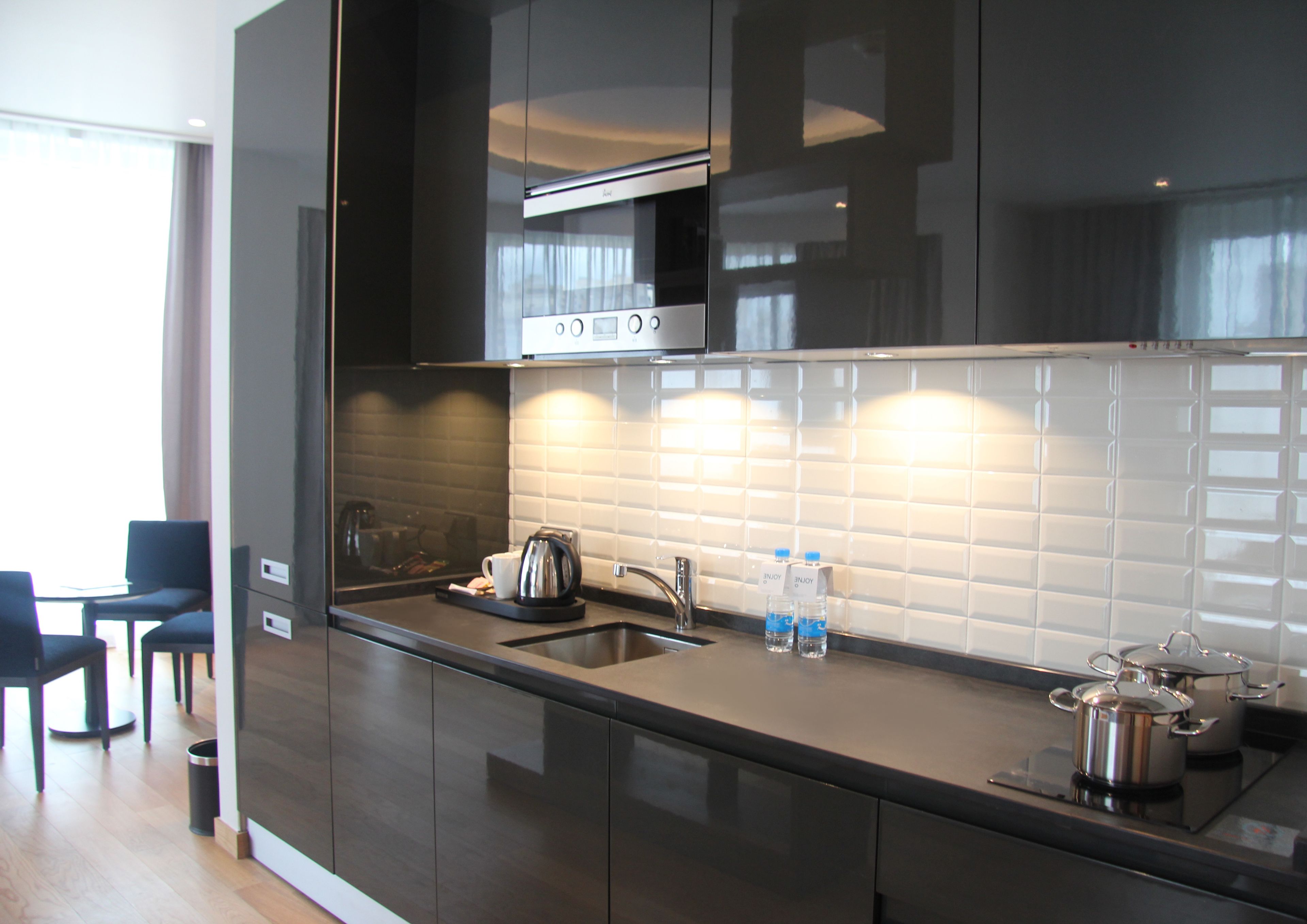 A modern kitchen with dark cabinetry, a stainless steel range hood, a sink, and a countertop with a kettle, water bottles, and pots.