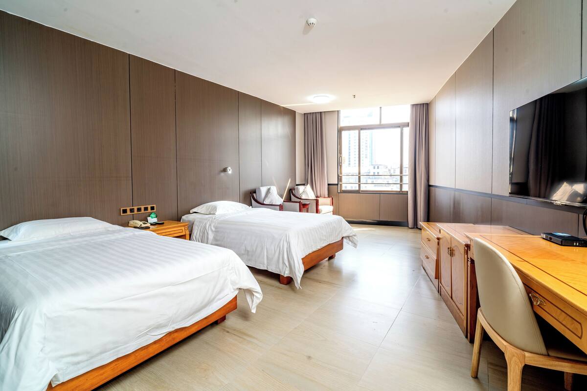 Ein Hotelzimmer mit zwei Betten, einem Schreibtisch, einem Stuhl, einem Fernseher und einem Fenster mit Vorhängen.