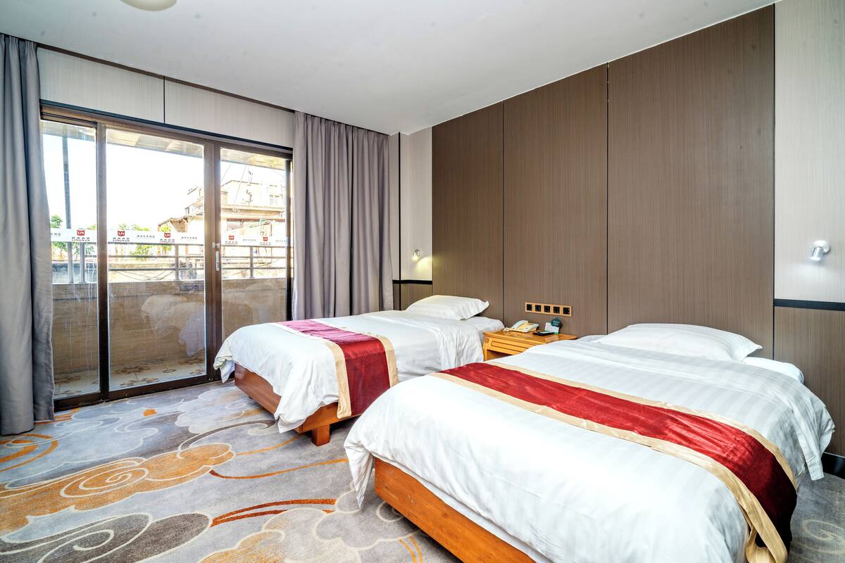 Ein Hotelzimmer mit zwei Betten, einer großen Schiebetür, einem Nachttisch und einer Lampe.