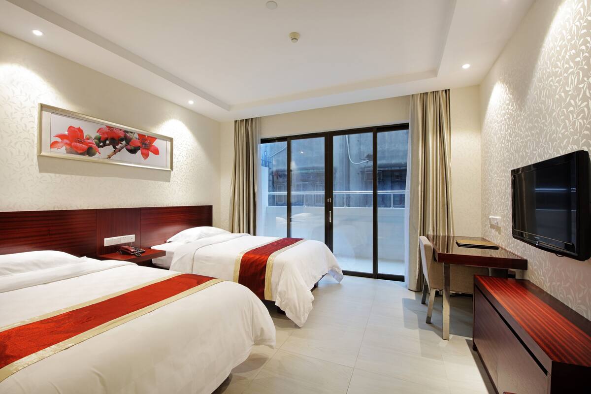 Ein Hotelzimmer mit zwei Betten, einem Schreibtisch, einem Fernseher und einem großen Fenster mit Blick.
