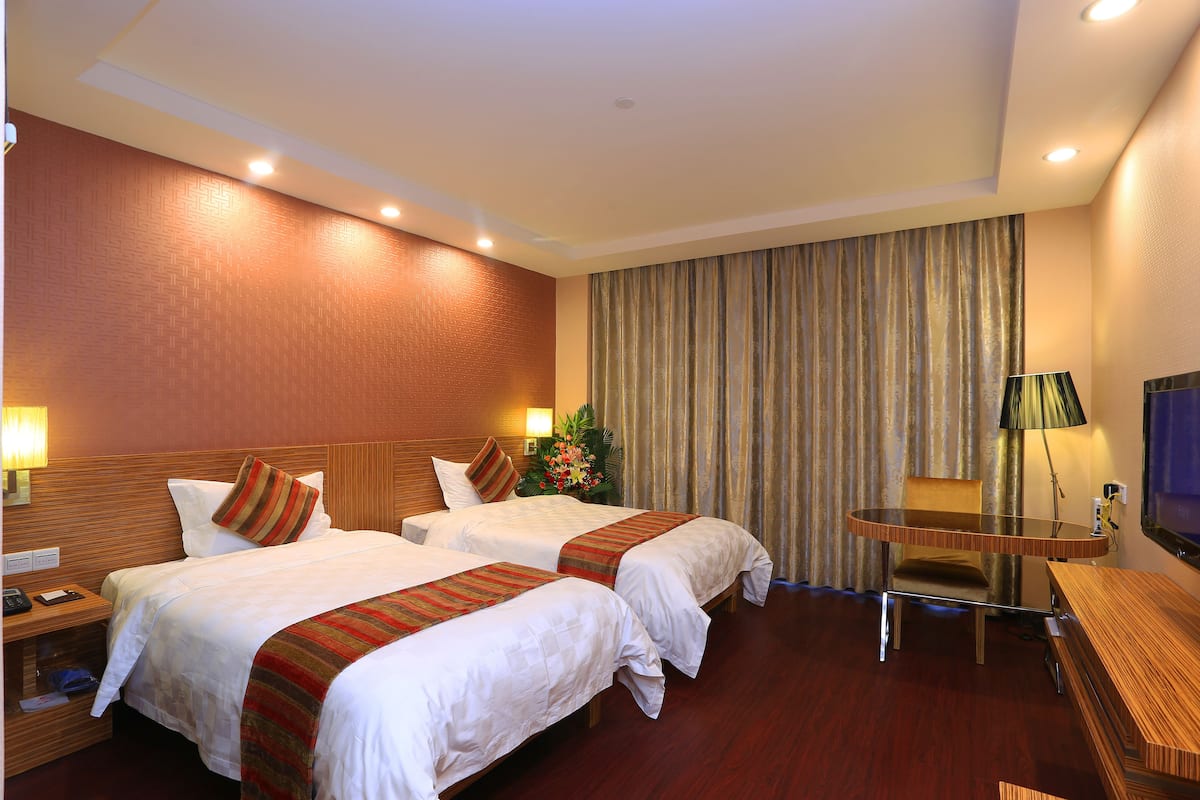 Ein Hotelzimmer mit zwei Betten, einem Schreibtisch, einem Sessel, einem Fernseher und einer Lampe.