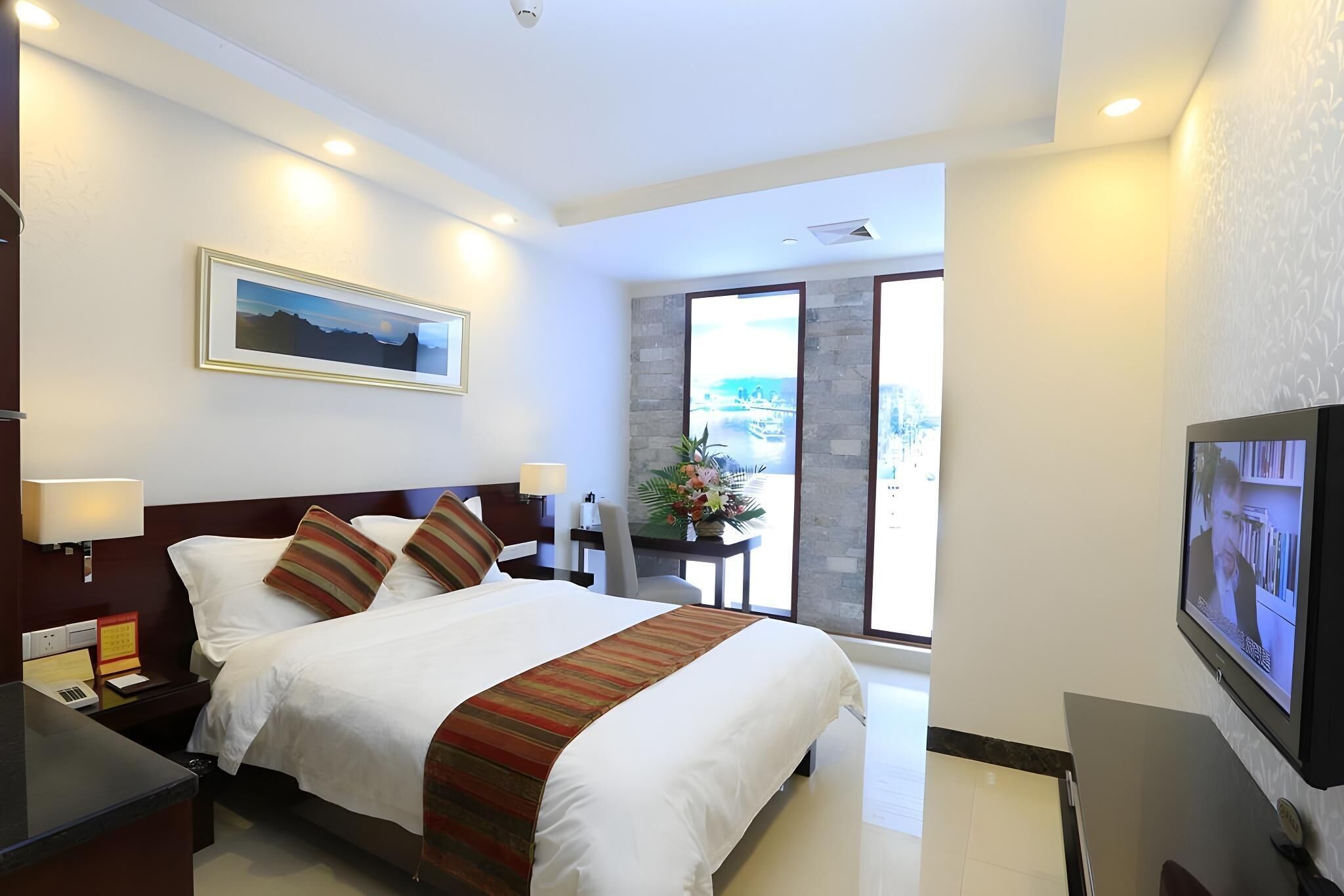 A hotel room with a large bed, a desk with a lamp, a television, and a view of the outdoors.