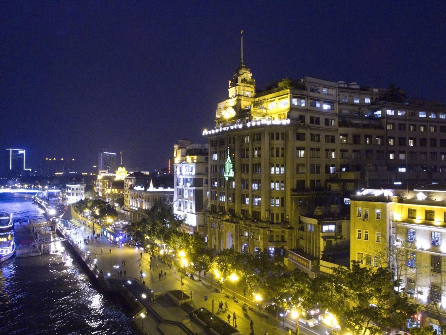 A nighttime view of a riverside cityscape with illuminated buildings, a prominent tower, and a bridge in the background.