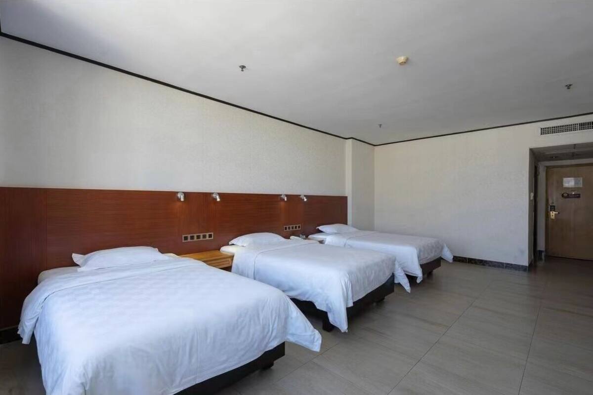 Ein Hotelzimmer mit drei Einzelbetten, einem Holzkopfende und einem Fliesenboden.