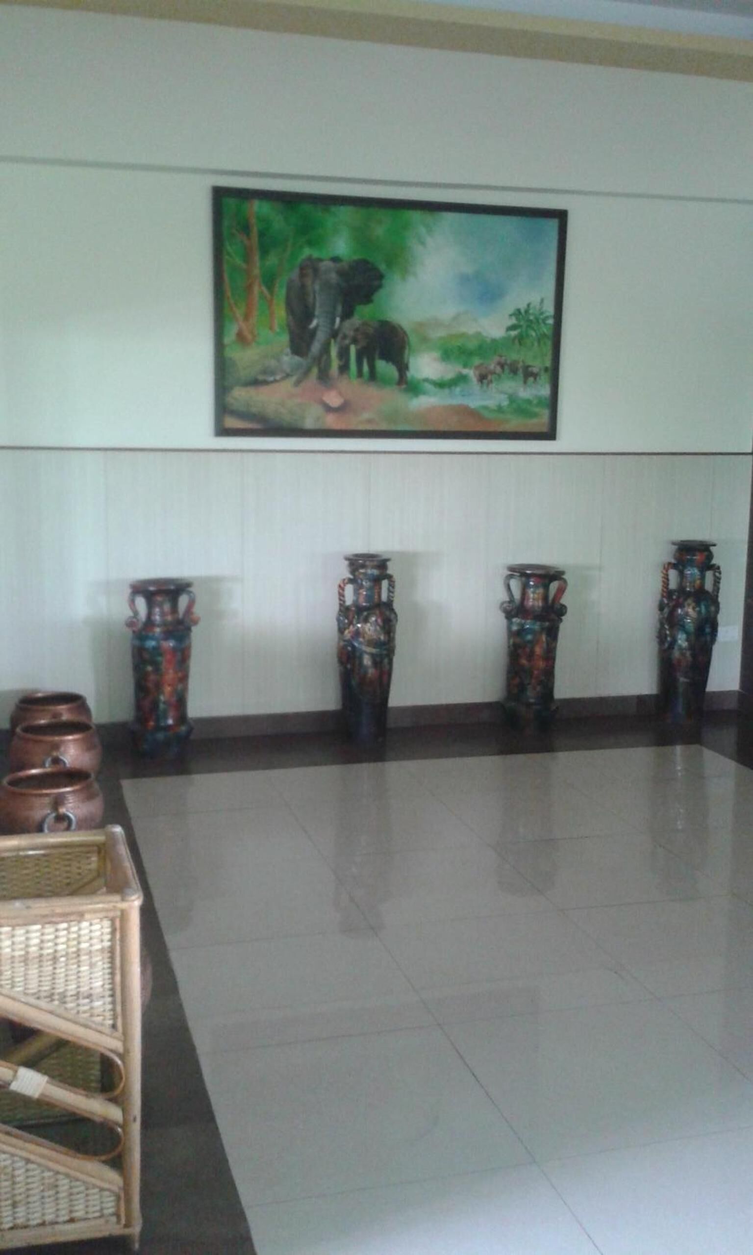A lobby with a large painting of elephants, a tiled floor, and several decorative vases.