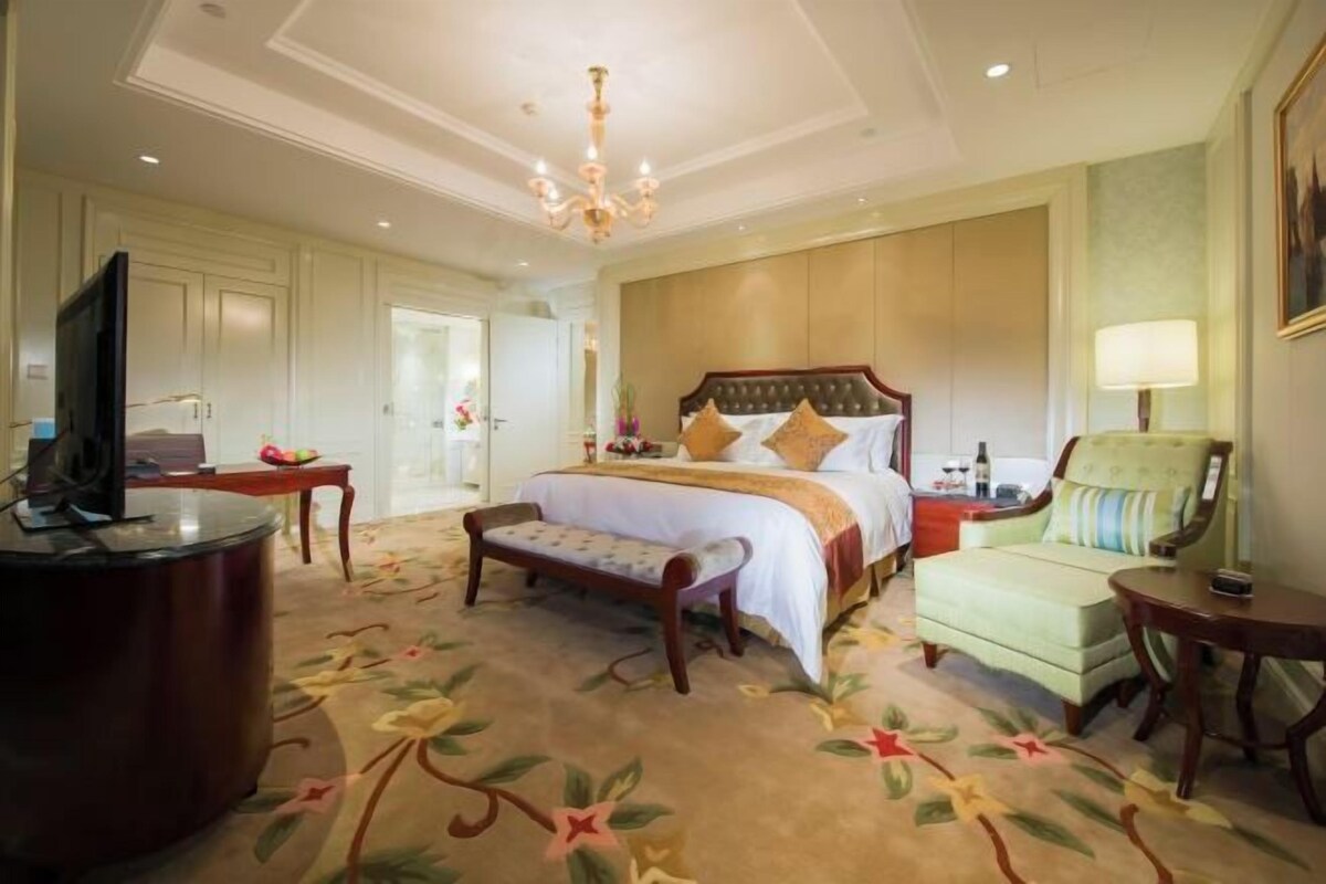 A hotel room with a large bed, a television, a bench, a chair, and a small table.