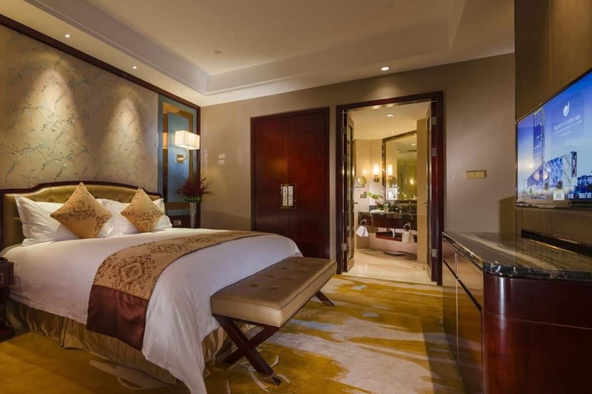 A modern hotel room with a large bed, bedside tables, a TV, and a bathroom visible through an open door.