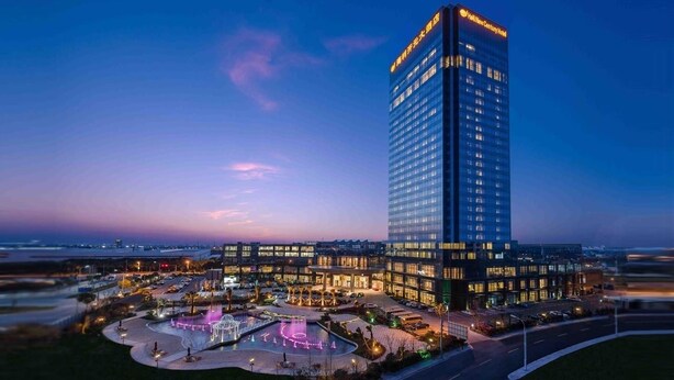 A high-rise hotel with a modern design, featuring a prominent entrance and a landscaped courtyard with a fountain.