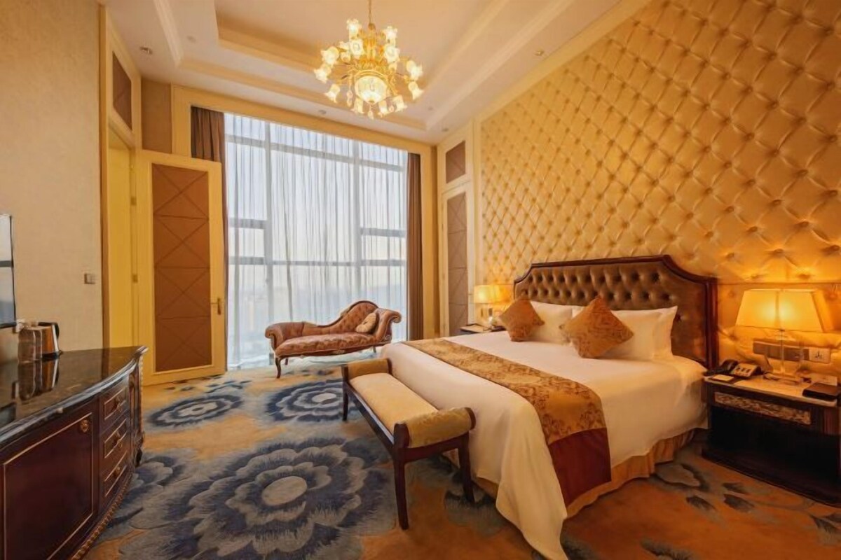 A hotel room with a large bed, a bench, a chair, a desk, and a chandelier.