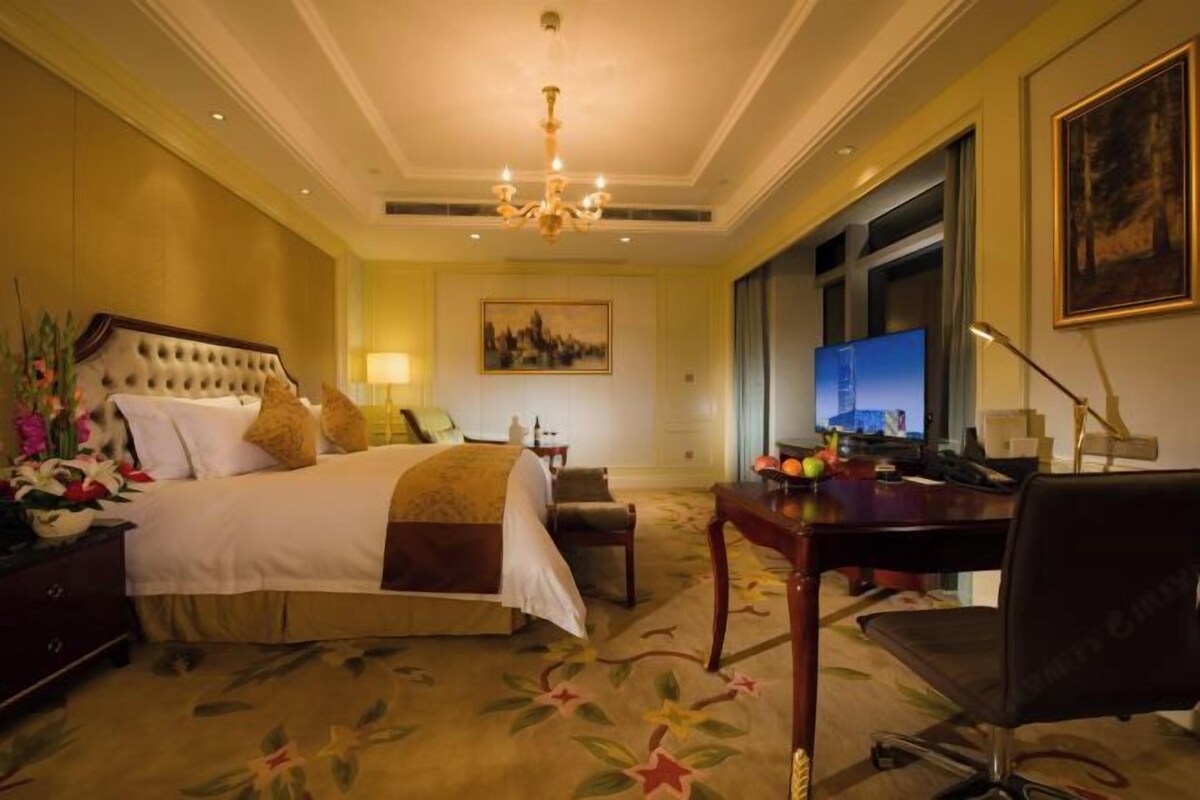 A hotel room with a large bed, a desk, a chair, a television, and a painting on the wall.