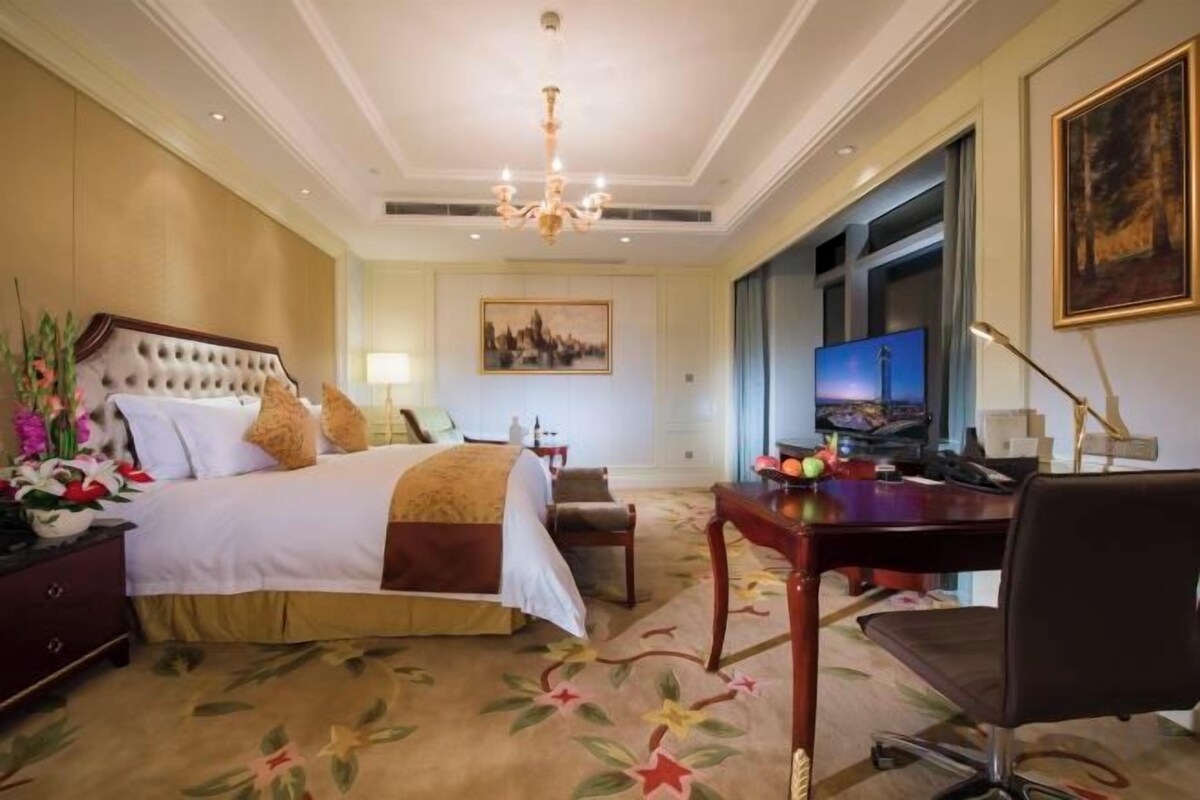 A hotel room with a large bed, a desk, a chair, a television, and a painting on the wall.