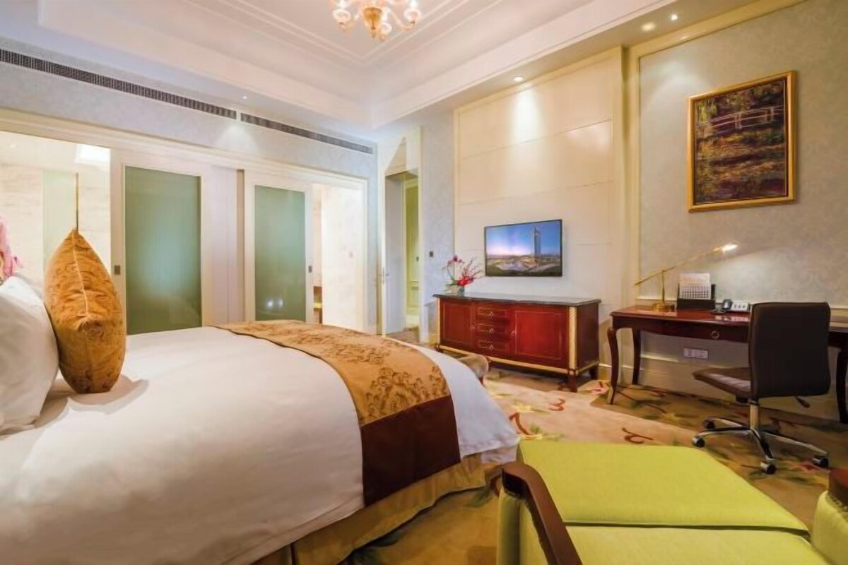A hotel room with a large bed, a desk with a computer, a chair, and a television on the wall.