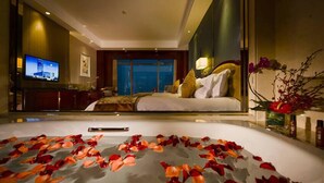 A hotel room with a large bed, a television, a desk, and a view of the cityscape.
