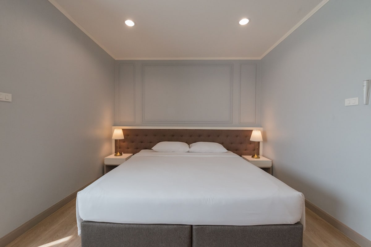Un cuarto de hotel ordenado con una cama grande, dos lámparas de noche y un cabecero acolchado.