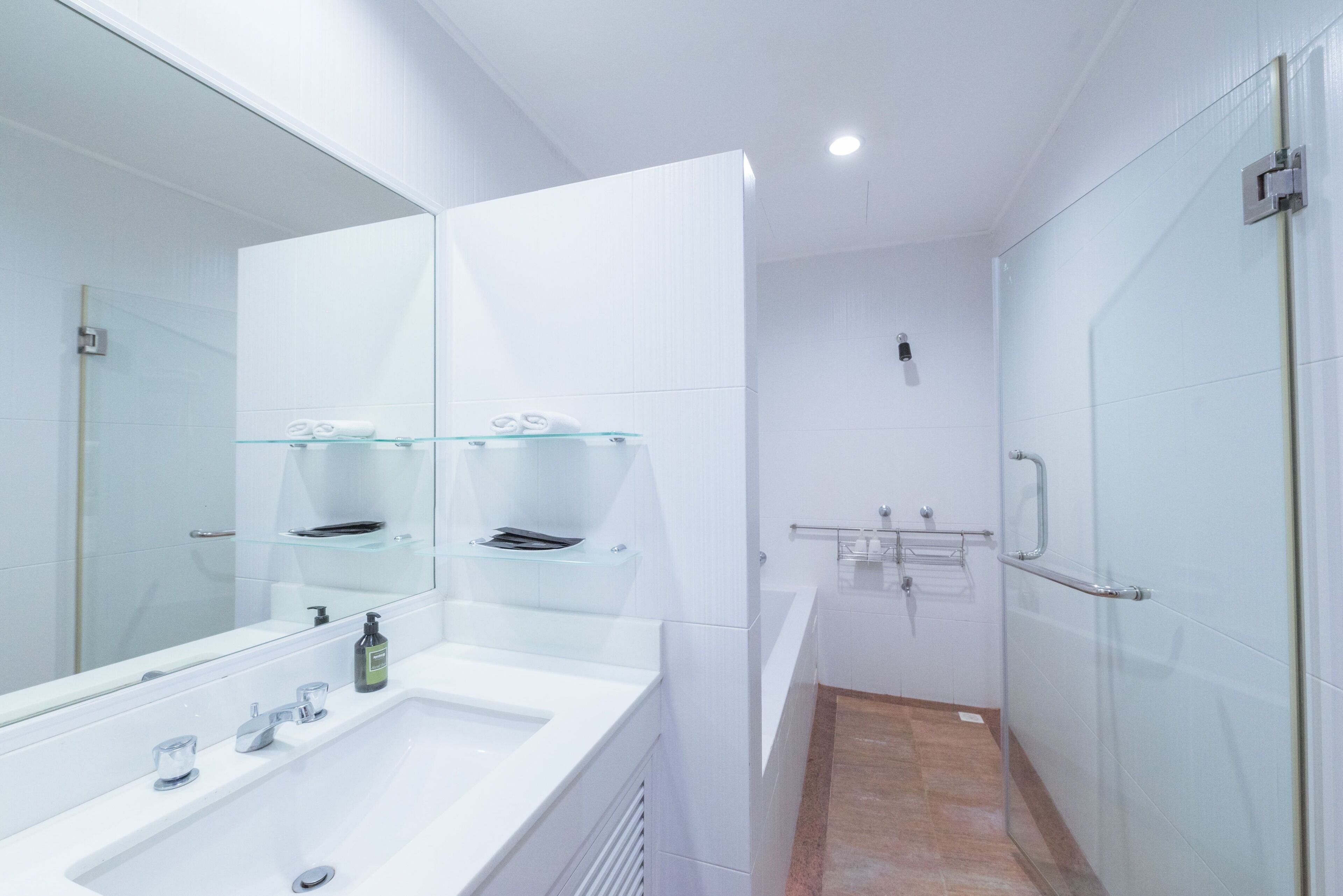A modern bathroom with a large mirror, a glass shelf, a sink, and a shower area.