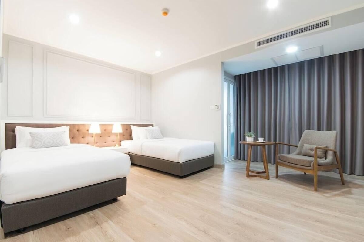 Habitación de hotel con dos camas, una mesita con una planta y una silla.
