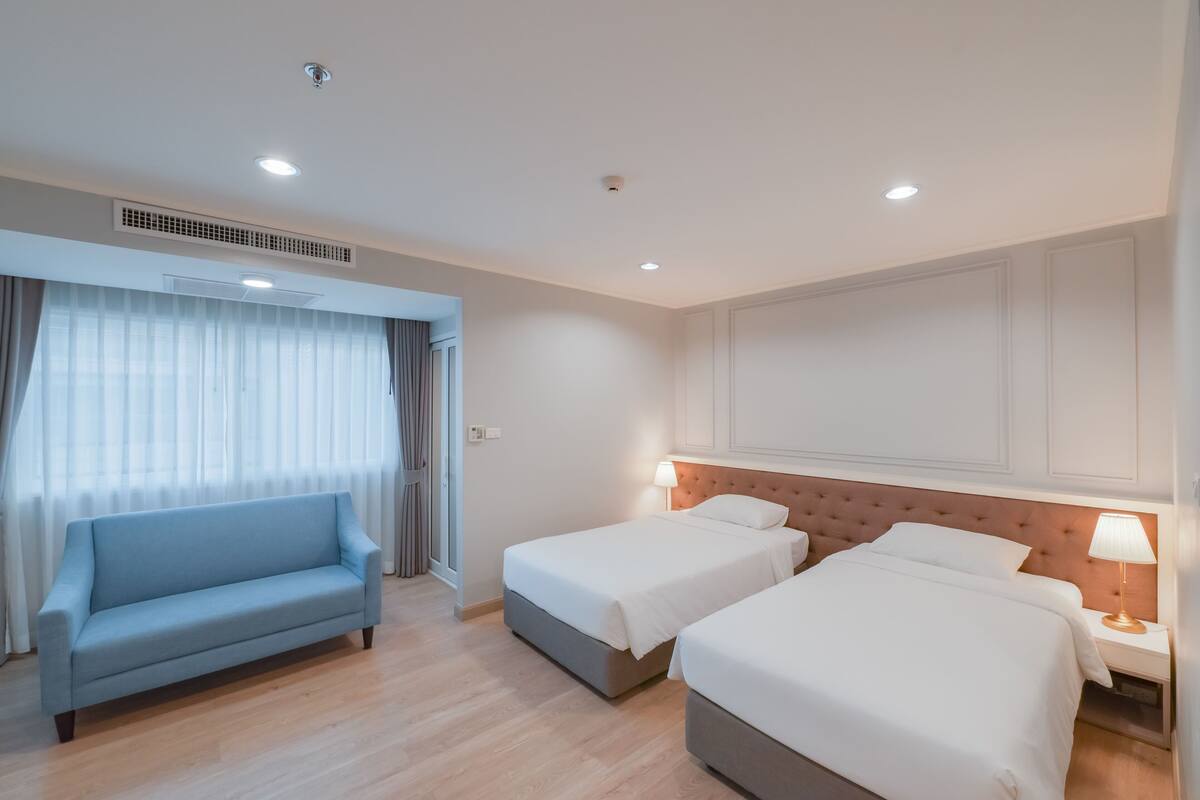 A hotel room with two beds, a sofa, and a large window with curtains.