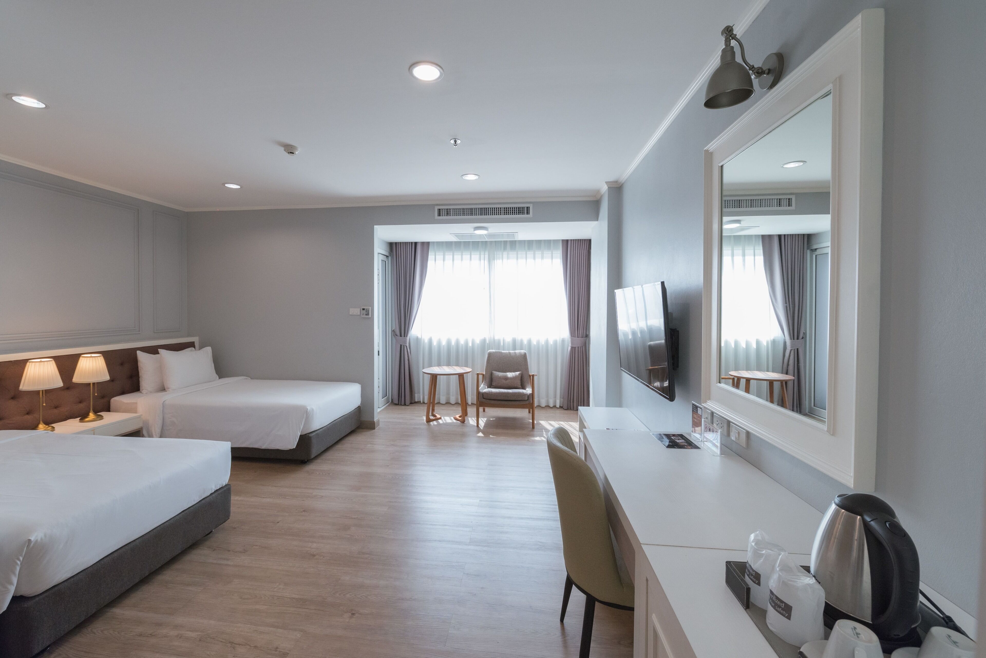 A hotel room with two beds, a desk, a chair, a television, and a large mirror.