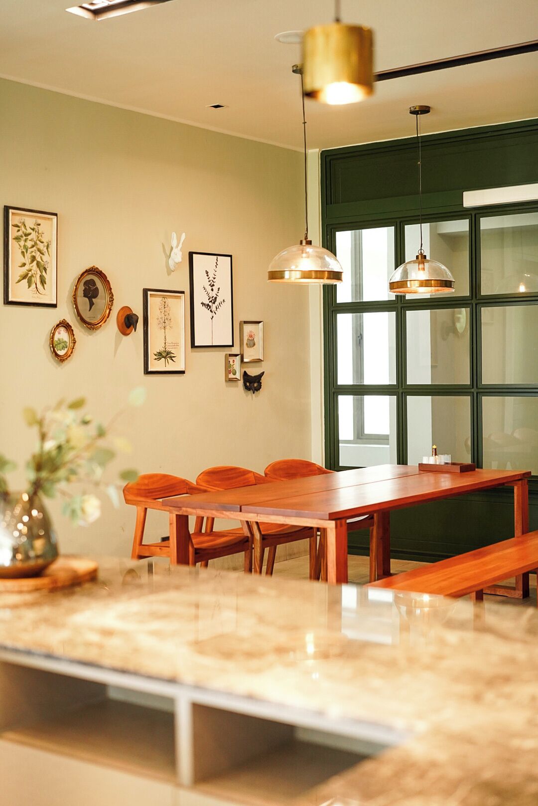 A dining area with a wooden table and chairs, a large window with green shutters, and wall-mounted pendant lights.