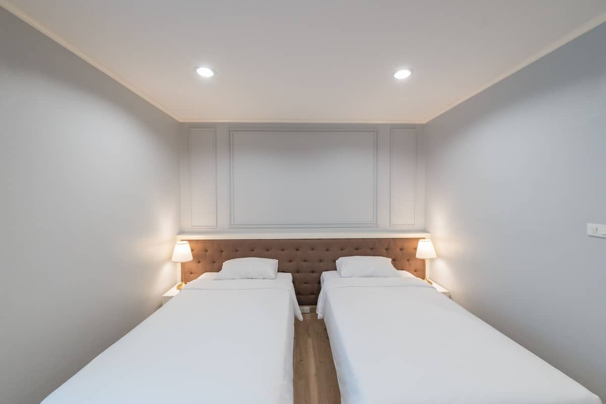 Una habitación de hotel con dos camas individuales, cabecero de madera, luces empotradas en el techo y lámparas de noche.