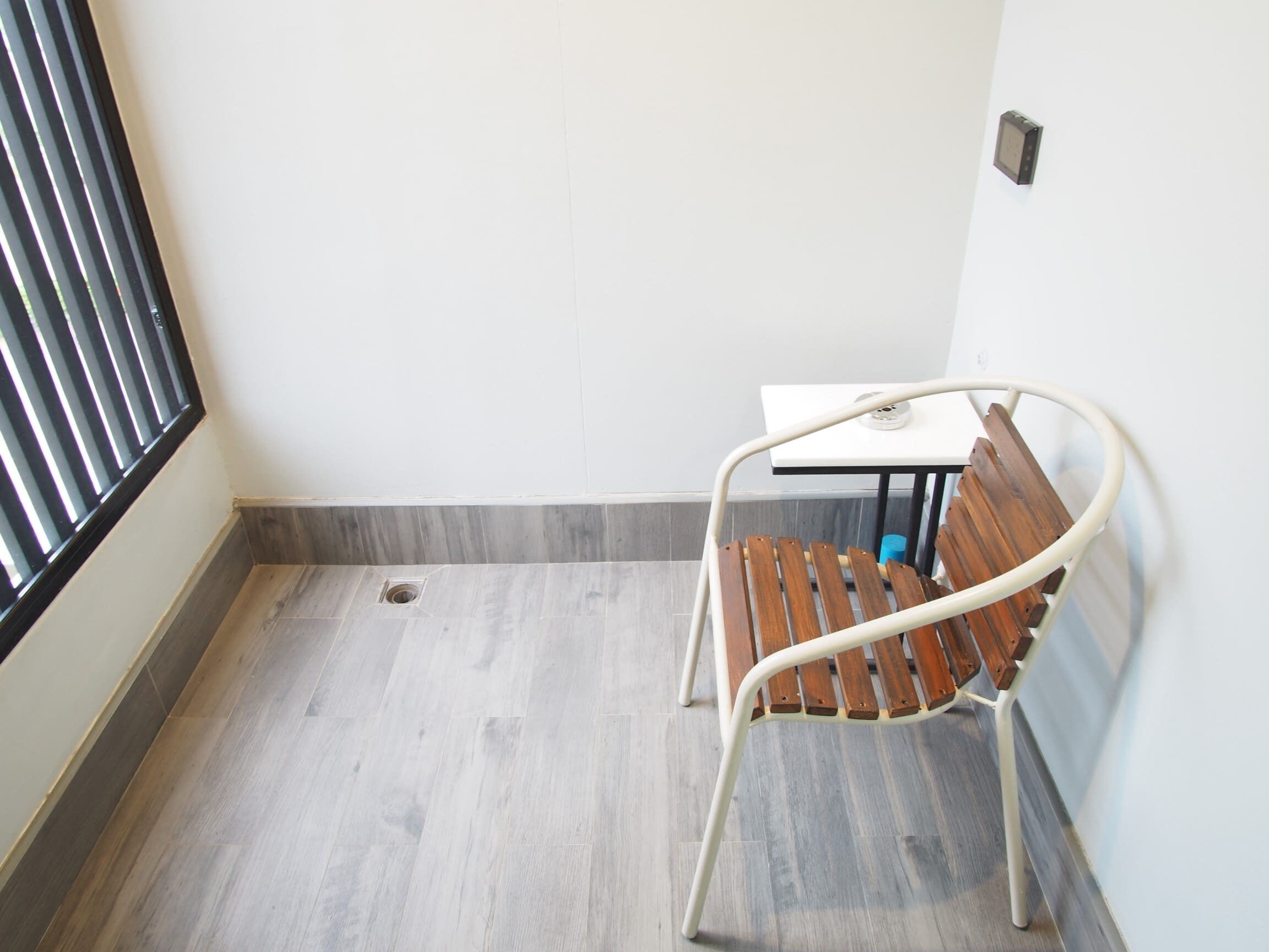 A corner room with a wooden bench, a small table, and a window with blinds.
