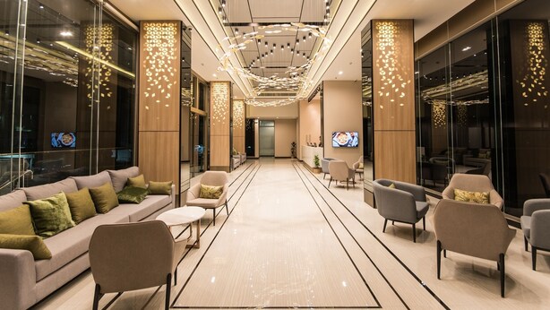 Un hall d’hôtel moderne doté d’un espace salon central, de murs en verre et d’un écran de télévision.