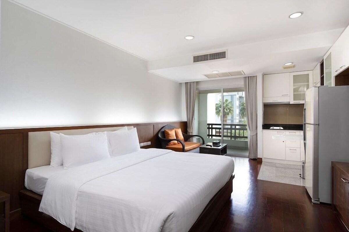 Ein Hotelzimmer mit einem großen Bett, einer Sitzecke mit einem Sessel, einer Küchenzeile und einem Balkon mit Blick.