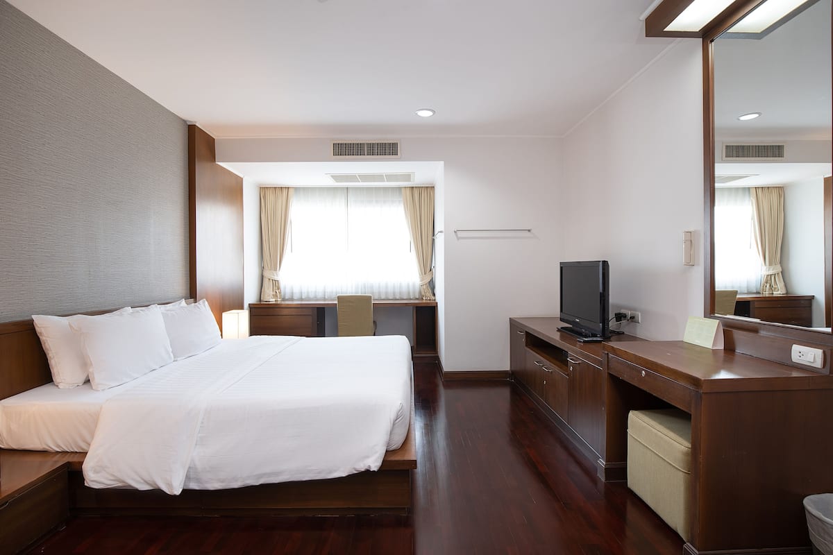 Una habitación de hotel con una cama grande, un escritorio, un televisor y un espejo.